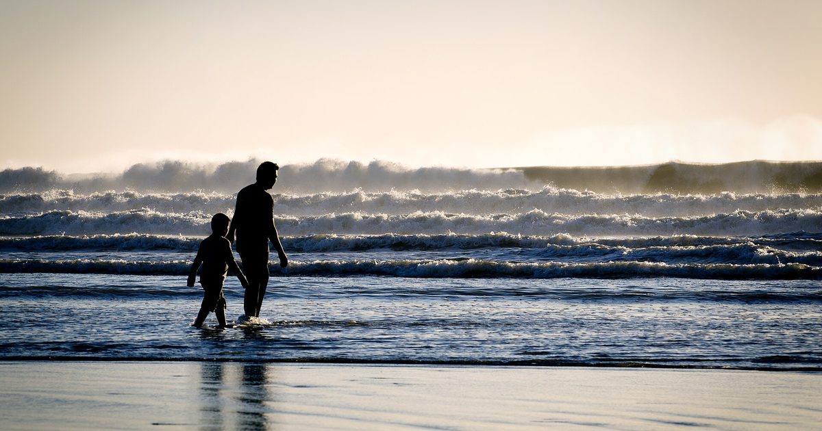 Silhouettes of an adult and a small child holding hands at the water's edge on a beach