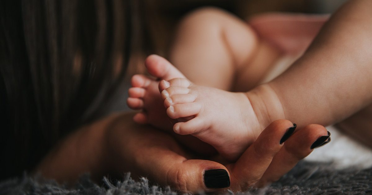 Parent's hand gently cradling a baby's bare feet on a soft blanket