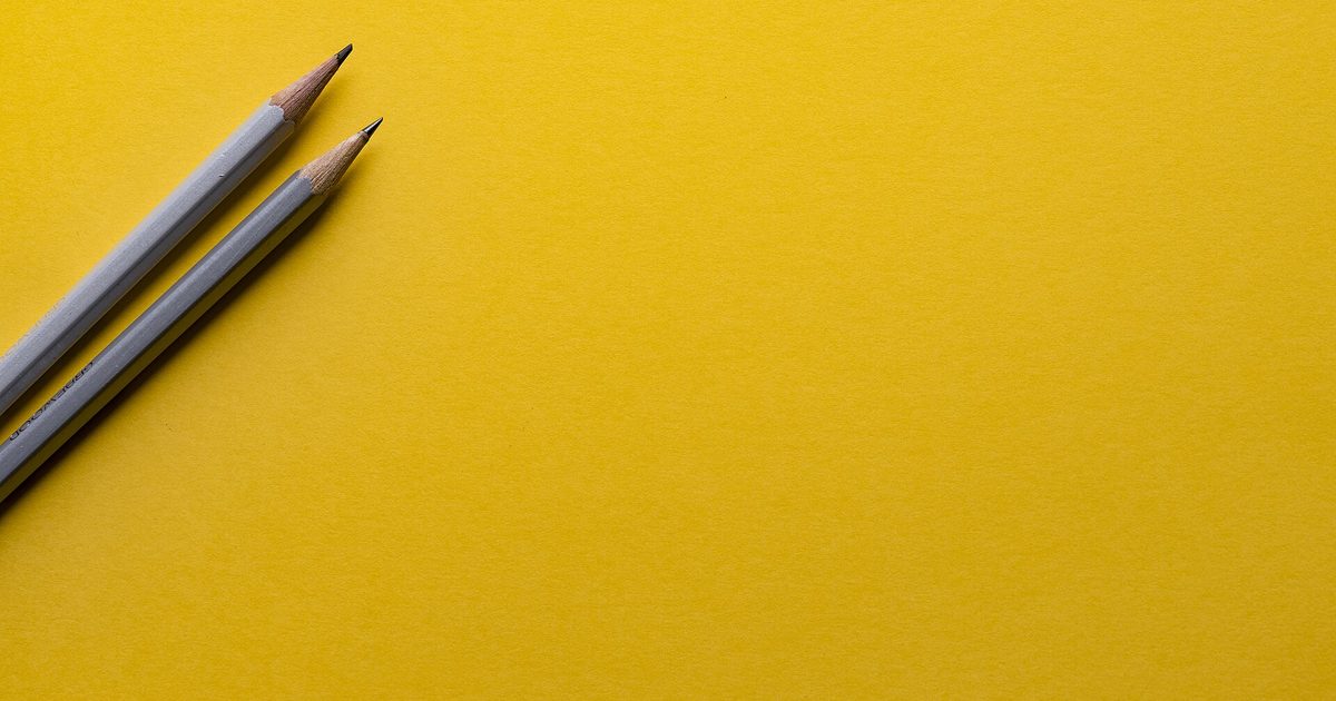 Two sharpened gray pencils lying on a plain bright yellow background