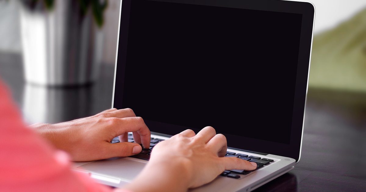 Close-up of a person's hands typing on a laptop keyboard at a desk