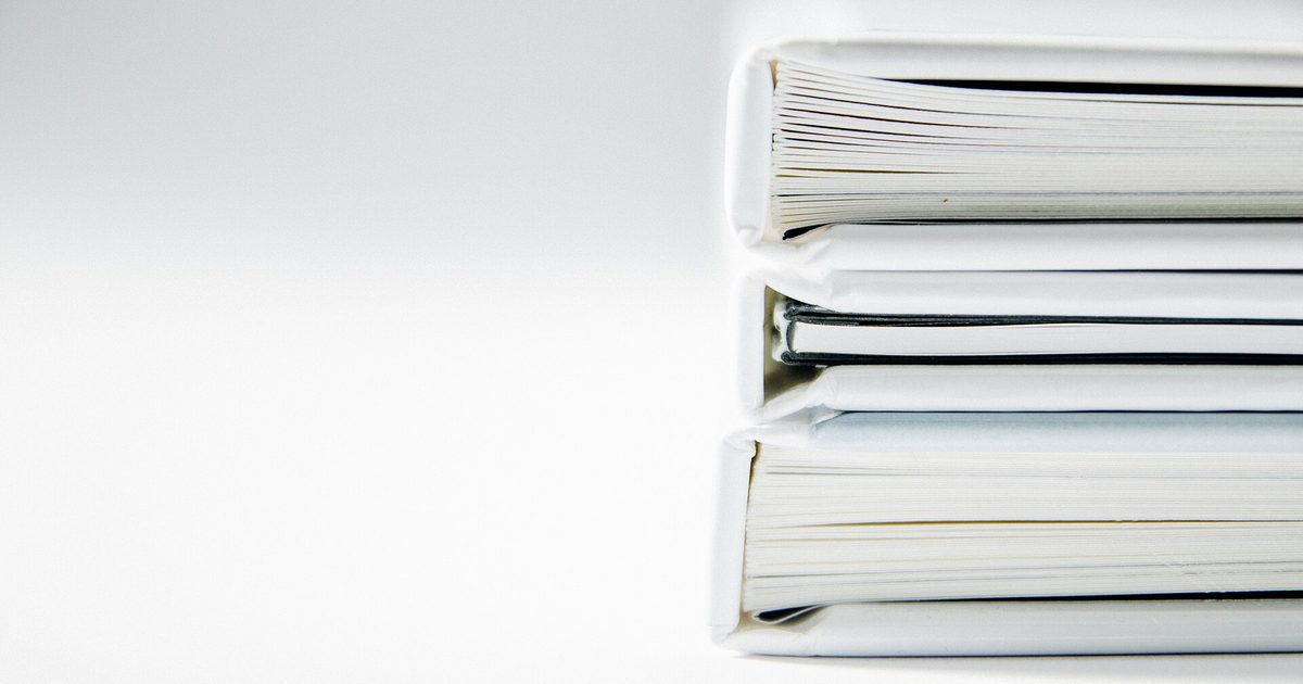 Stack of white ring binders lying on a plain white surface, spines toward the viewer