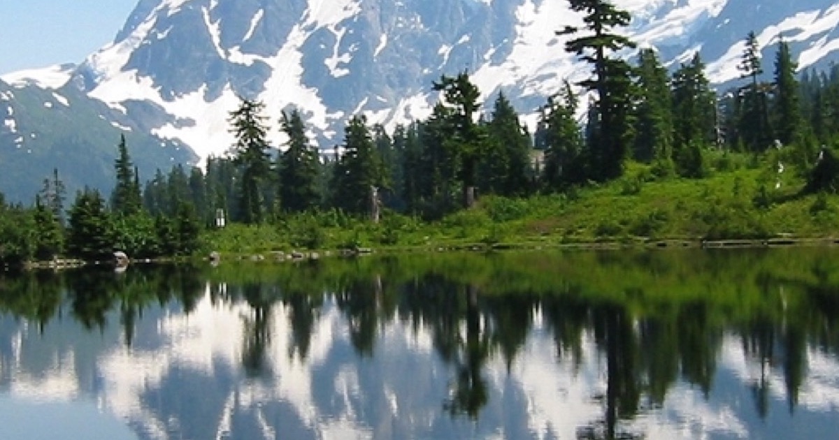 A snow-capped mountain range and evergreen forest reflected in a still alpine lake