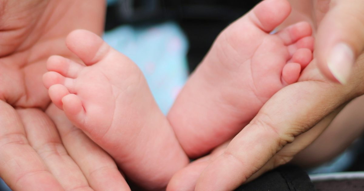 Adult hands gently cradling the tiny bare feet of a newborn baby