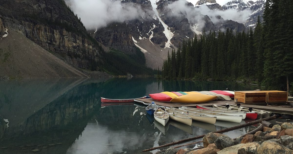 Colorful kayaks and canoes moored on a still mountain lake beside a rocky shore