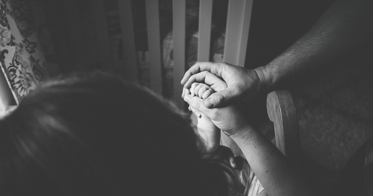 Black-and-white close-up of a child's hand held between a mother's and father's hands