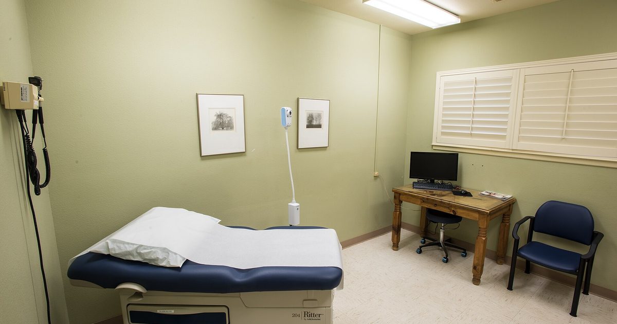 An empty examination room in a community health clinic with an exam table, sink and supplies
