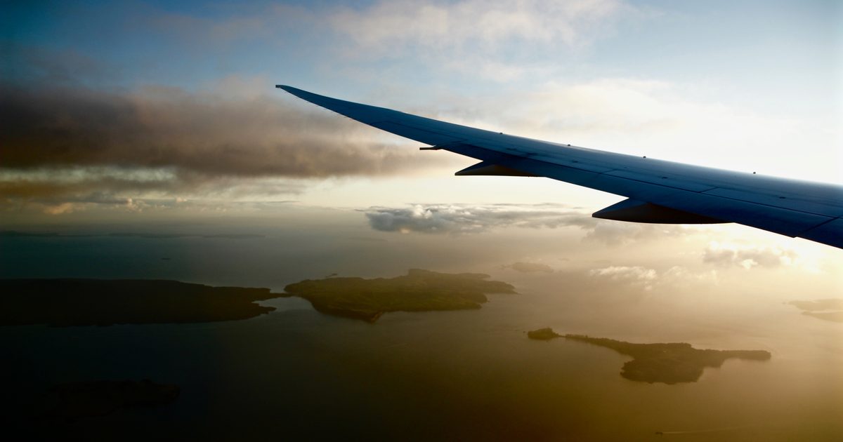 Airplane wing seen from a window seat high above green islands and a hazy sea
